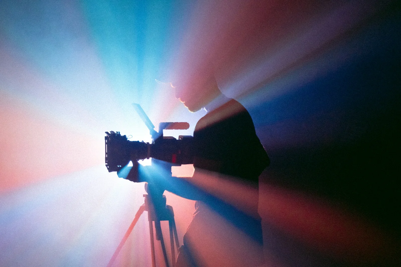 Silhouette d’une personne filmant avec une caméra sur trépied, dans une lumière bleue et rouge