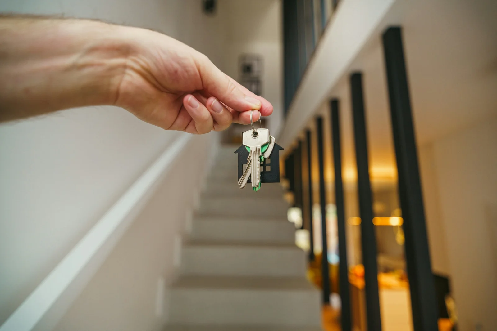 Main tendant des clés avec un porte-clés en forme de maison